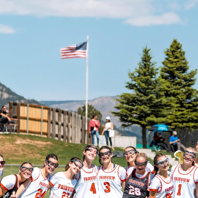Fairview Knights lacrosse team posing together with goggles on, mountains and American flag in the background